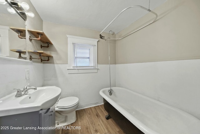 full bathroom with toilet, a bath, wood finished floors, vanity, and tile walls