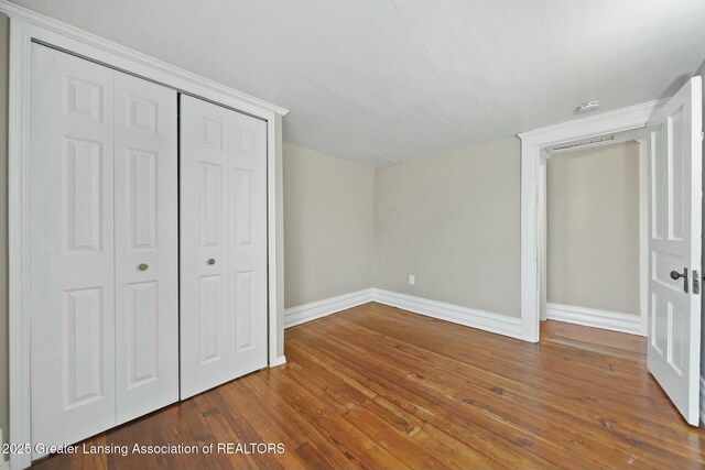 unfurnished bedroom featuring hardwood / wood-style floors, a closet, and baseboards