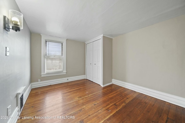 unfurnished bedroom with hardwood / wood-style floors, a closet, visible vents, and baseboards