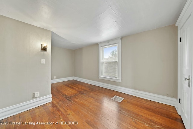 spare room with baseboards, visible vents, and hardwood / wood-style floors