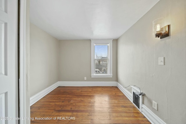 spare room with wood finished floors, visible vents, and baseboards