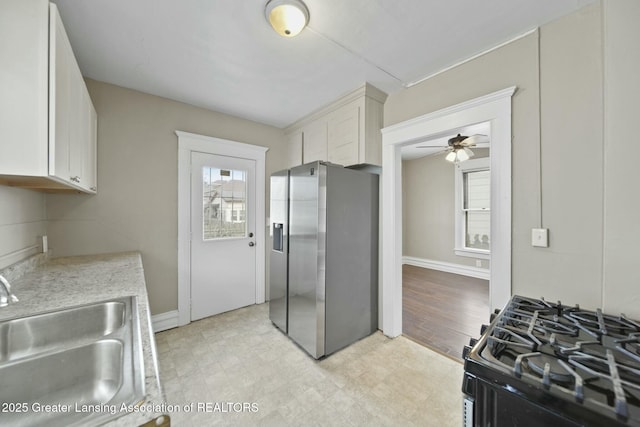 kitchen with baseboards, light floors, stainless steel refrigerator with ice dispenser, a sink, and gas stove