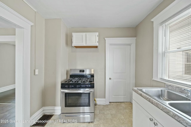 kitchen featuring light countertops, white cabinets, a sink, gas range, and baseboards