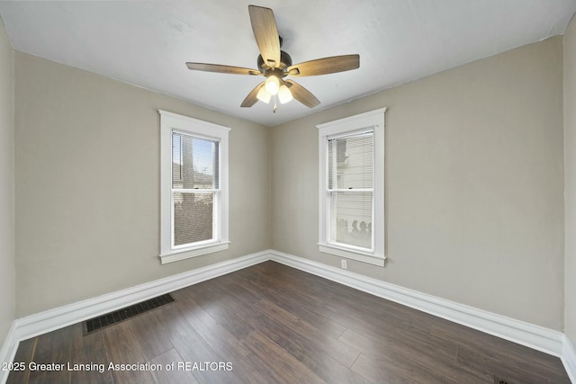 unfurnished room featuring dark wood-type flooring, a healthy amount of sunlight, visible vents, and baseboards