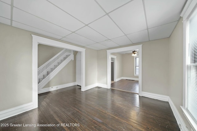 unfurnished room featuring a paneled ceiling, wood-type flooring, stairs, and baseboards