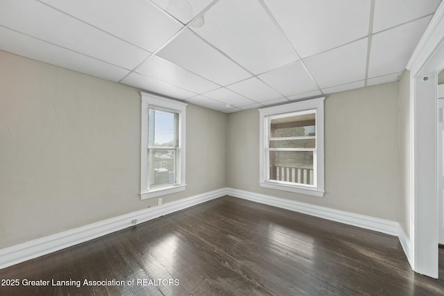 empty room with a paneled ceiling, baseboards, and hardwood / wood-style flooring