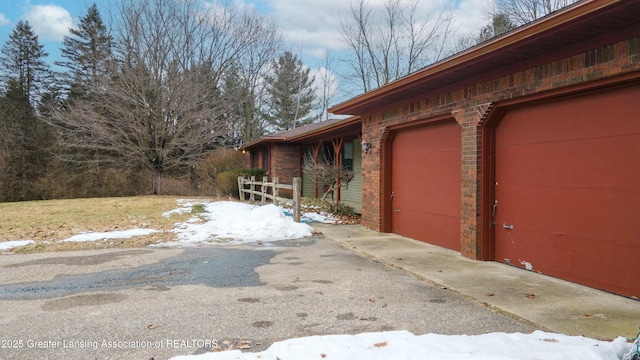 view of snow covered exterior featuring driveway, a garage, and brick siding