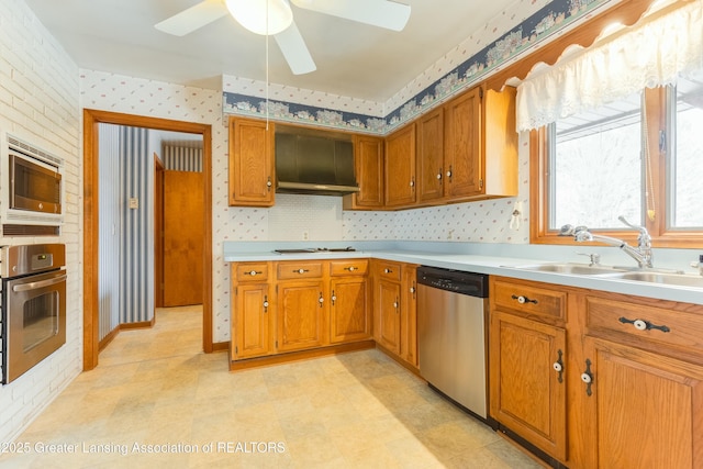 kitchen featuring appliances with stainless steel finishes, brown cabinets, a sink, and wallpapered walls