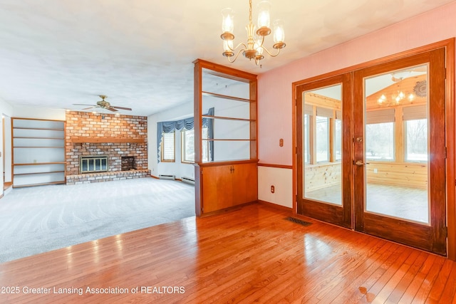 interior space featuring visible vents, hardwood / wood-style floors, french doors, a fireplace, and ceiling fan with notable chandelier