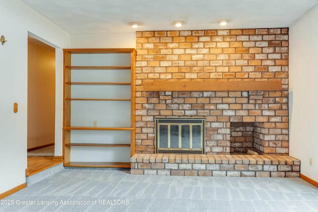 unfurnished living room featuring a brick fireplace, carpet flooring, and baseboards