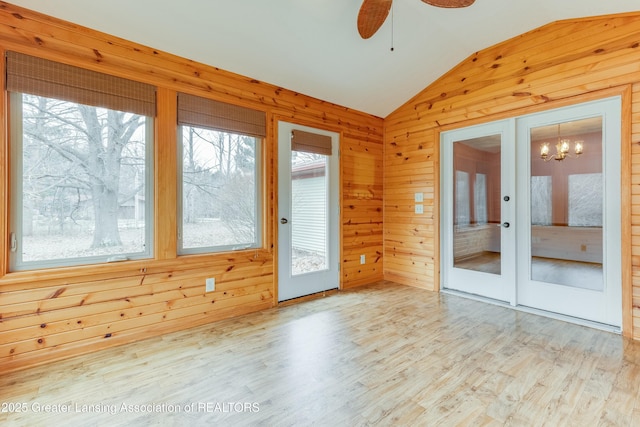 unfurnished room with lofted ceiling, ceiling fan with notable chandelier, wood walls, wood finished floors, and french doors