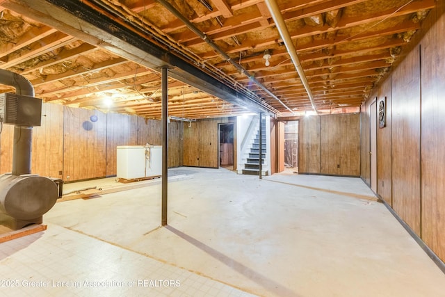 unfinished basement featuring stairs, wood walls, and fridge