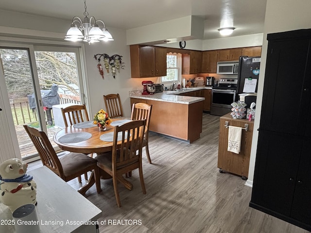 kitchen with light wood finished floors, a peninsula, an inviting chandelier, stainless steel appliances, and light countertops