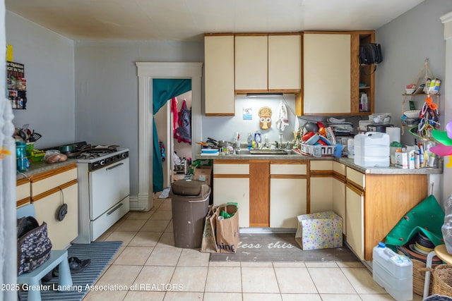 kitchen featuring light tile patterned floors, a peninsula, light countertops, cream cabinetry, and gas range oven