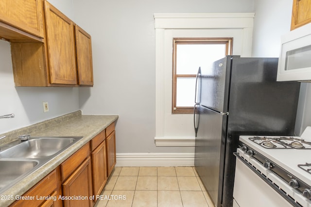 kitchen with light tile patterned floors, white appliances, brown cabinetry, and a sink