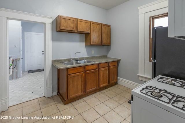 kitchen featuring a sink, brown cabinets, white gas stove, and freestanding refrigerator