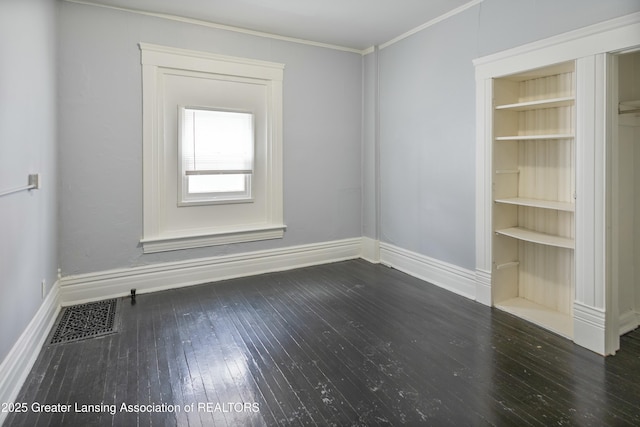 spare room featuring visible vents, built in shelves, baseboards, ornamental molding, and hardwood / wood-style flooring