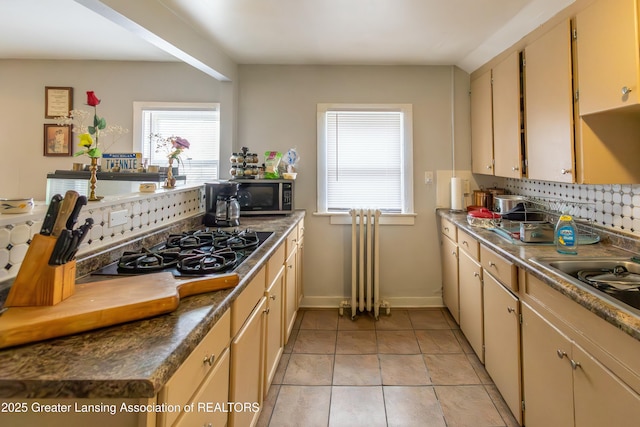 kitchen with black gas stovetop, stainless steel microwave, backsplash, light tile patterned flooring, and baseboards