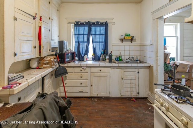 kitchen featuring dark wood-type flooring, tile countertops, white gas range, decorative backsplash, and a sink