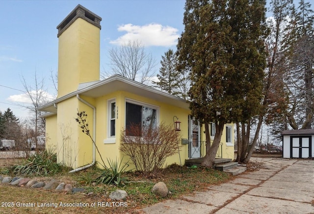 exterior space with an outbuilding, a shed, a chimney, and stucco siding