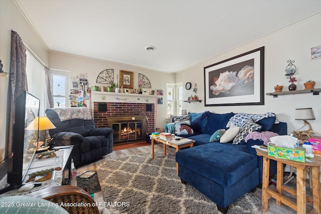 living room featuring a brick fireplace, wood finished floors, visible vents, and crown molding