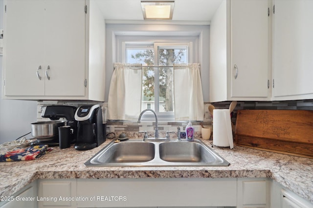 kitchen featuring white cabinets, light countertops, a sink, and backsplash