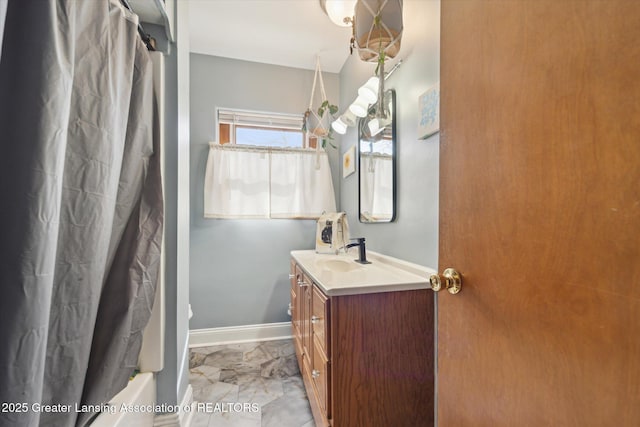 full bathroom with marble finish floor, baseboards, shower / bath combo with shower curtain, and vanity