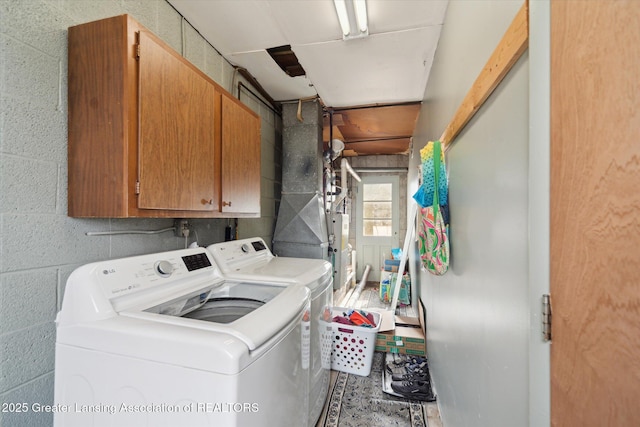 washroom featuring concrete block wall, cabinet space, and washing machine and clothes dryer