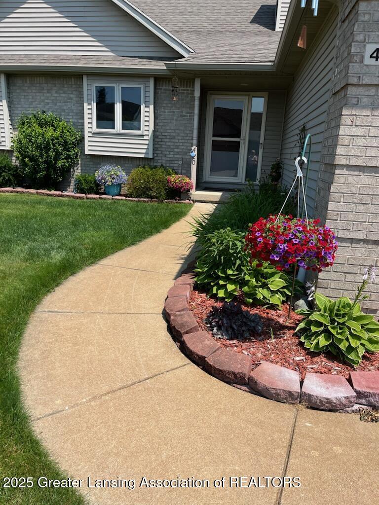 entrance to property with roof with shingles, a lawn, and brick siding