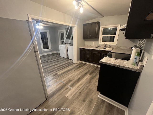 kitchen featuring washer and clothes dryer, a sink, freestanding refrigerator, light stone countertops, and dark wood-style flooring