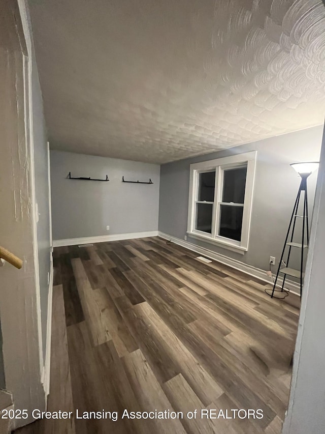 unfurnished room with a textured ceiling, baseboards, and wood finished floors