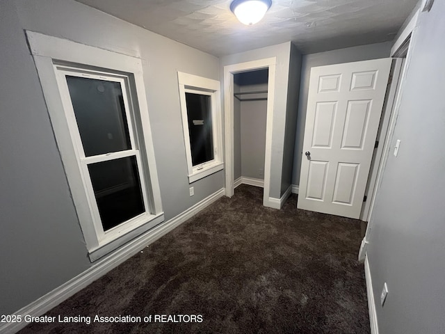 unfurnished bedroom featuring a closet, baseboards, and dark carpet