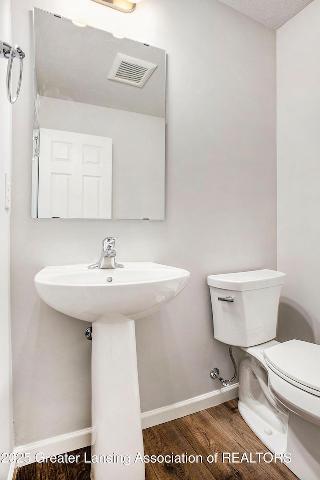 bathroom with baseboards, visible vents, toilet, and wood finished floors