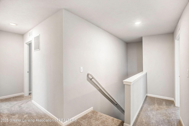 hallway featuring carpet, visible vents, baseboards, and an upstairs landing