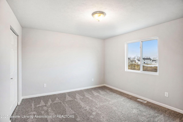 carpeted spare room with a textured ceiling, visible vents, and baseboards