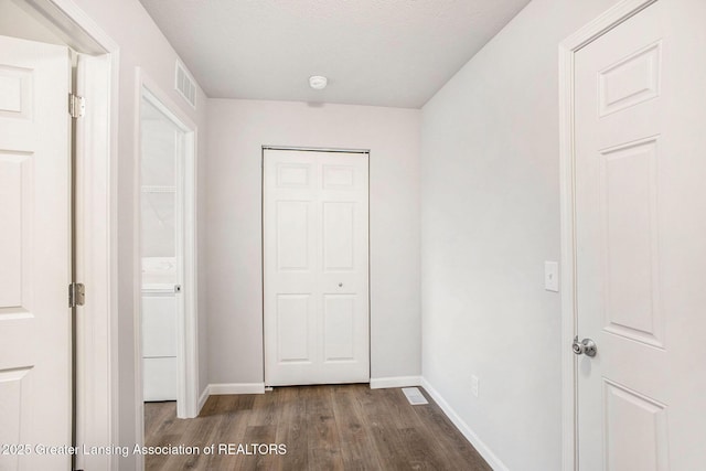 hall featuring dark wood-type flooring, visible vents, a textured ceiling, and baseboards