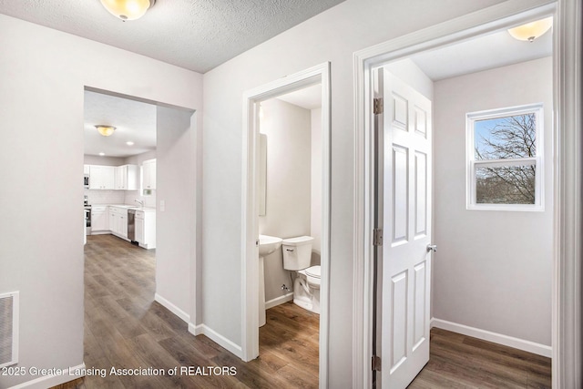 hallway featuring dark wood-style flooring, visible vents, a textured ceiling, and baseboards