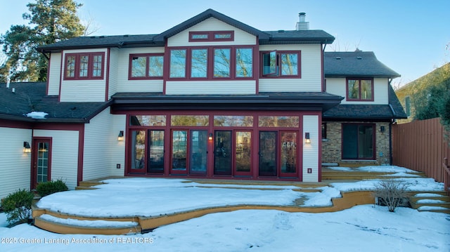 snow covered back of property with french doors, fence, a chimney, and a patio