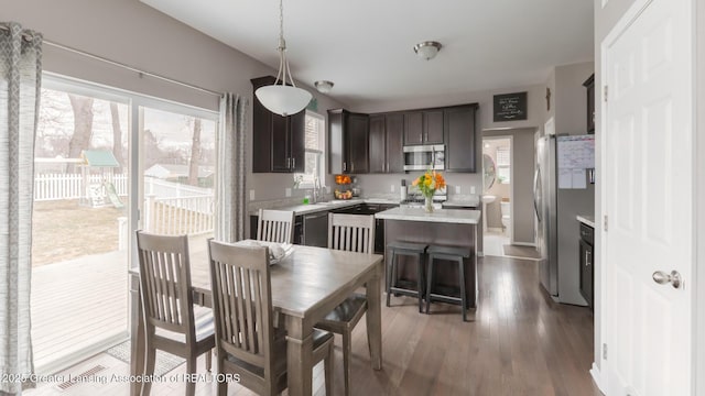 kitchen featuring appliances with stainless steel finishes, a center island, light countertops, dark brown cabinets, and a sink