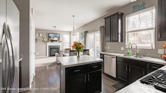 kitchen with stainless steel appliances, a sink, light countertops, a center island, and a glass covered fireplace