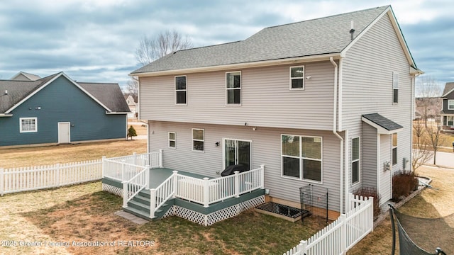 rear view of property featuring a fenced backyard, a deck, a shingled roof, and a yard