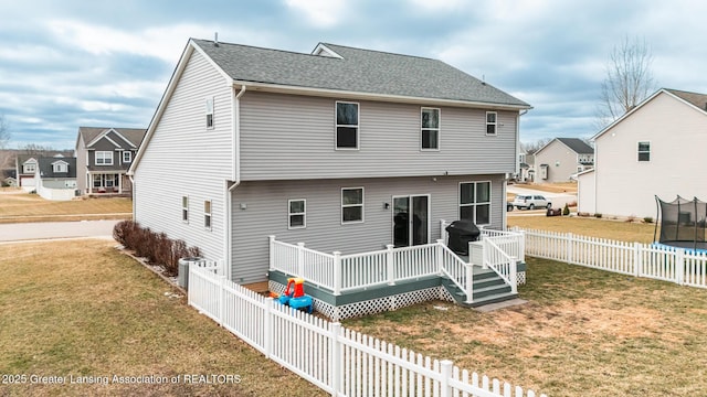 rear view of property featuring a trampoline, a wooden deck, a lawn, and a fenced backyard