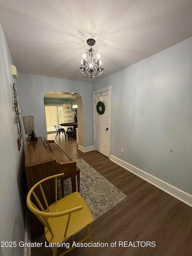 interior space with arched walkways, a textured ceiling, a notable chandelier, wood finished floors, and baseboards