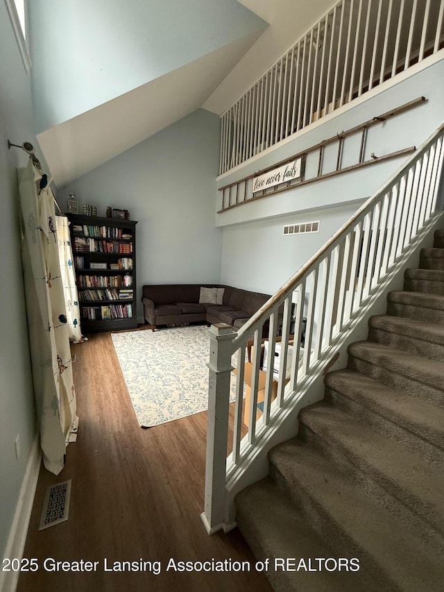 stairway featuring lofted ceiling, visible vents, and wood finished floors