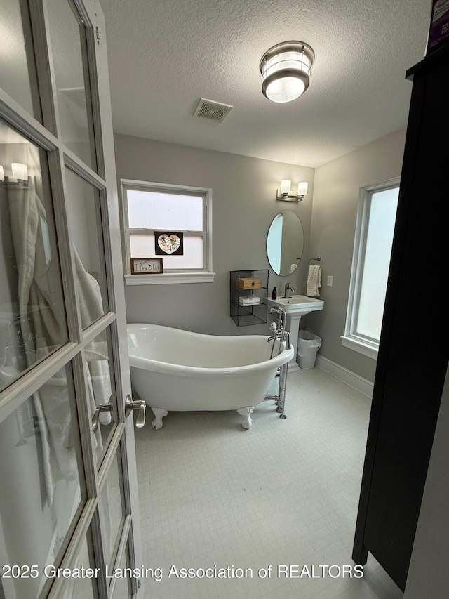 full bathroom featuring a freestanding bath, a textured ceiling, and baseboards