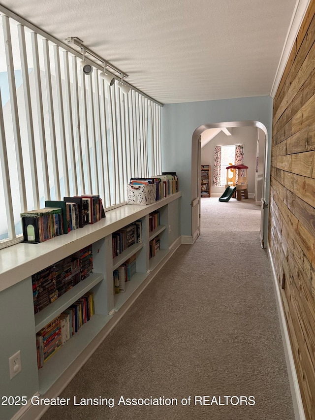 corridor featuring arched walkways, carpet flooring, and a textured ceiling