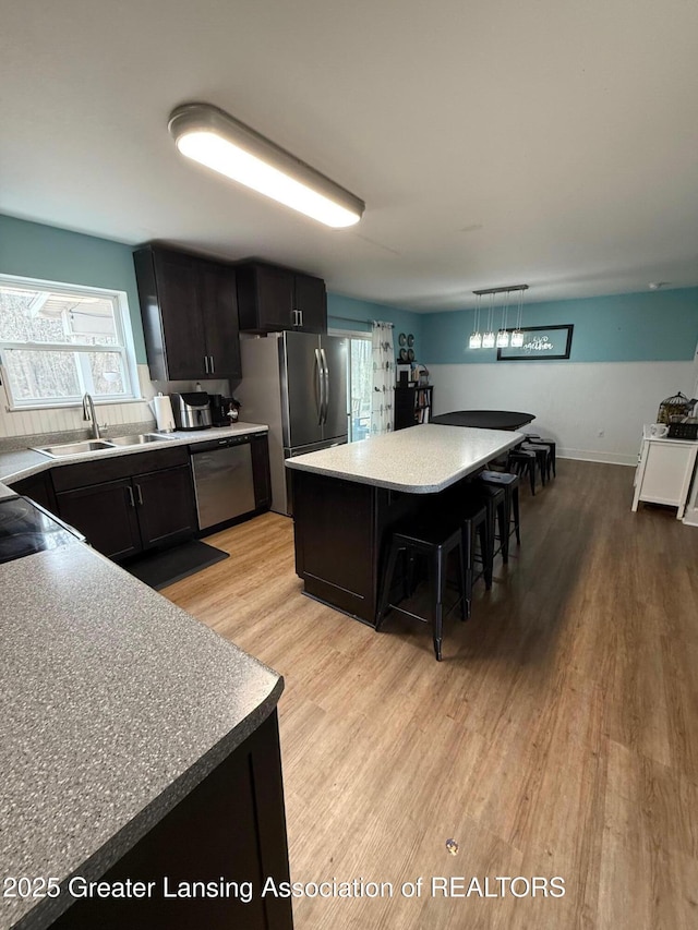 kitchen with a breakfast bar, light countertops, light wood-style flooring, appliances with stainless steel finishes, and a sink