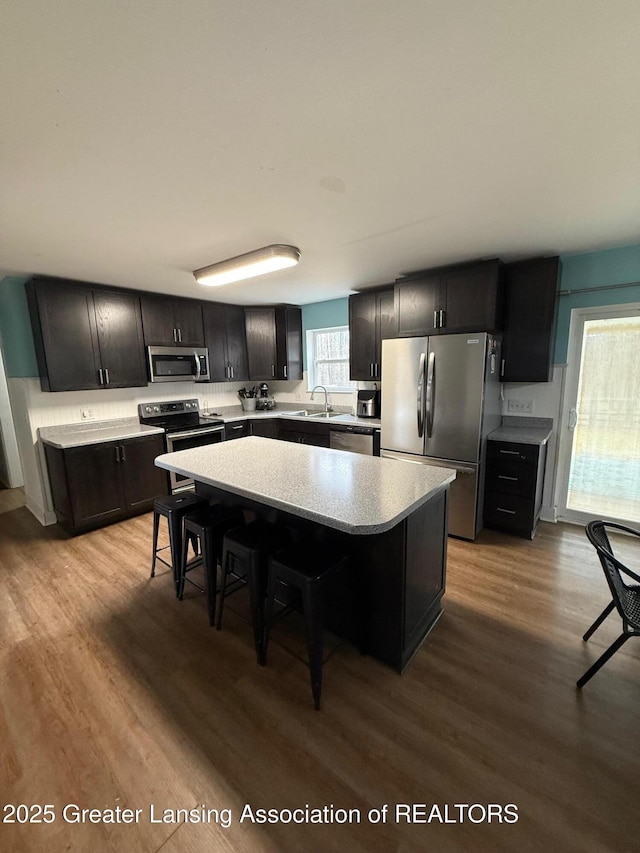 kitchen with a breakfast bar area, wood finished floors, a center island, stainless steel appliances, and light countertops