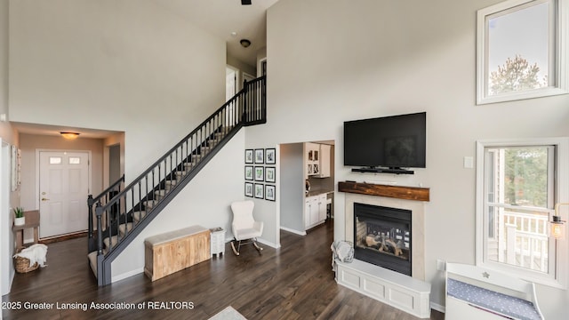 living area with a towering ceiling, stairs, baseboards, and dark wood finished floors