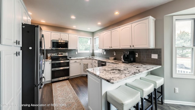 kitchen with decorative backsplash, a peninsula, stainless steel appliances, white cabinetry, and a sink